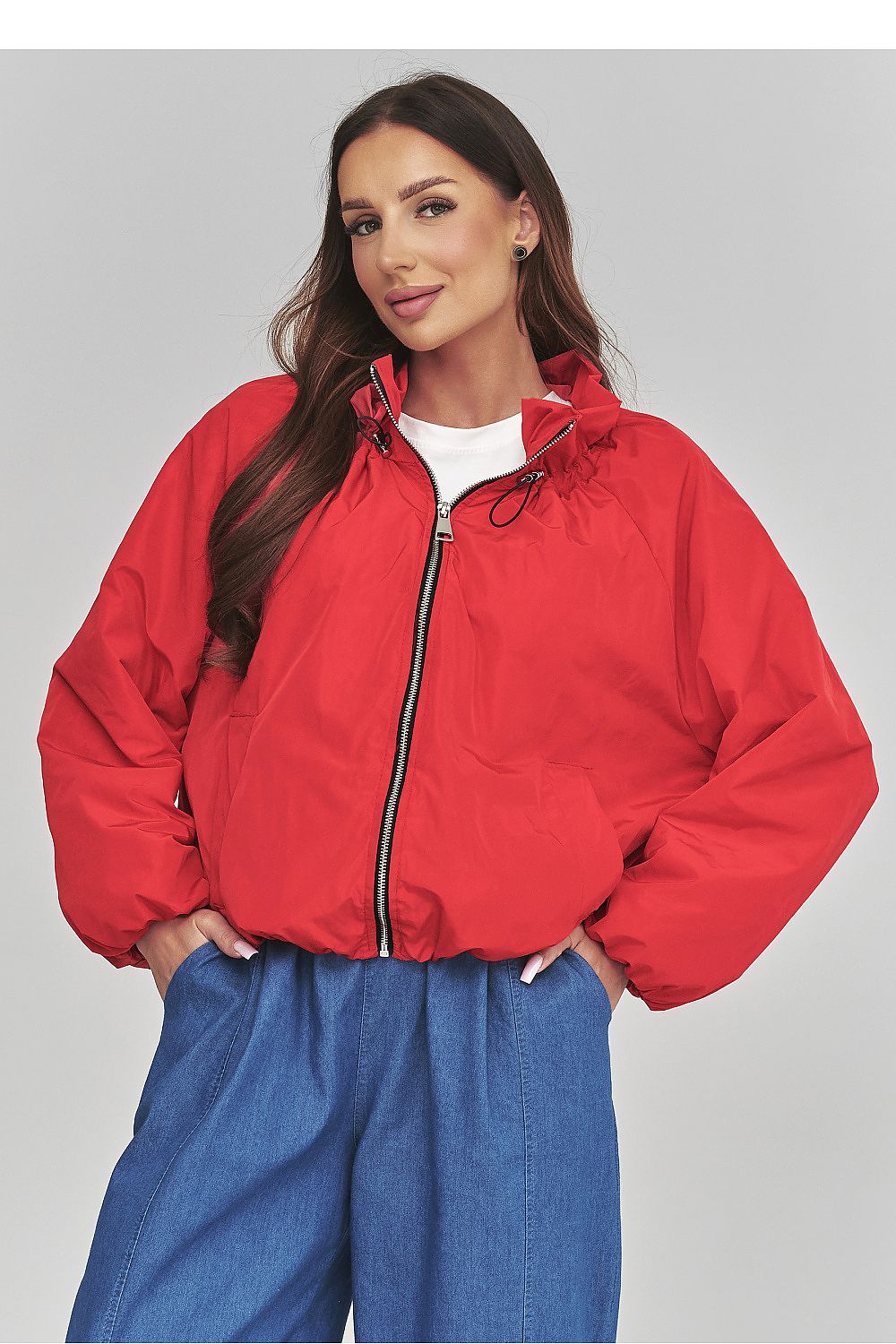 Woman wearing a red jacket and blue pants on a gray background