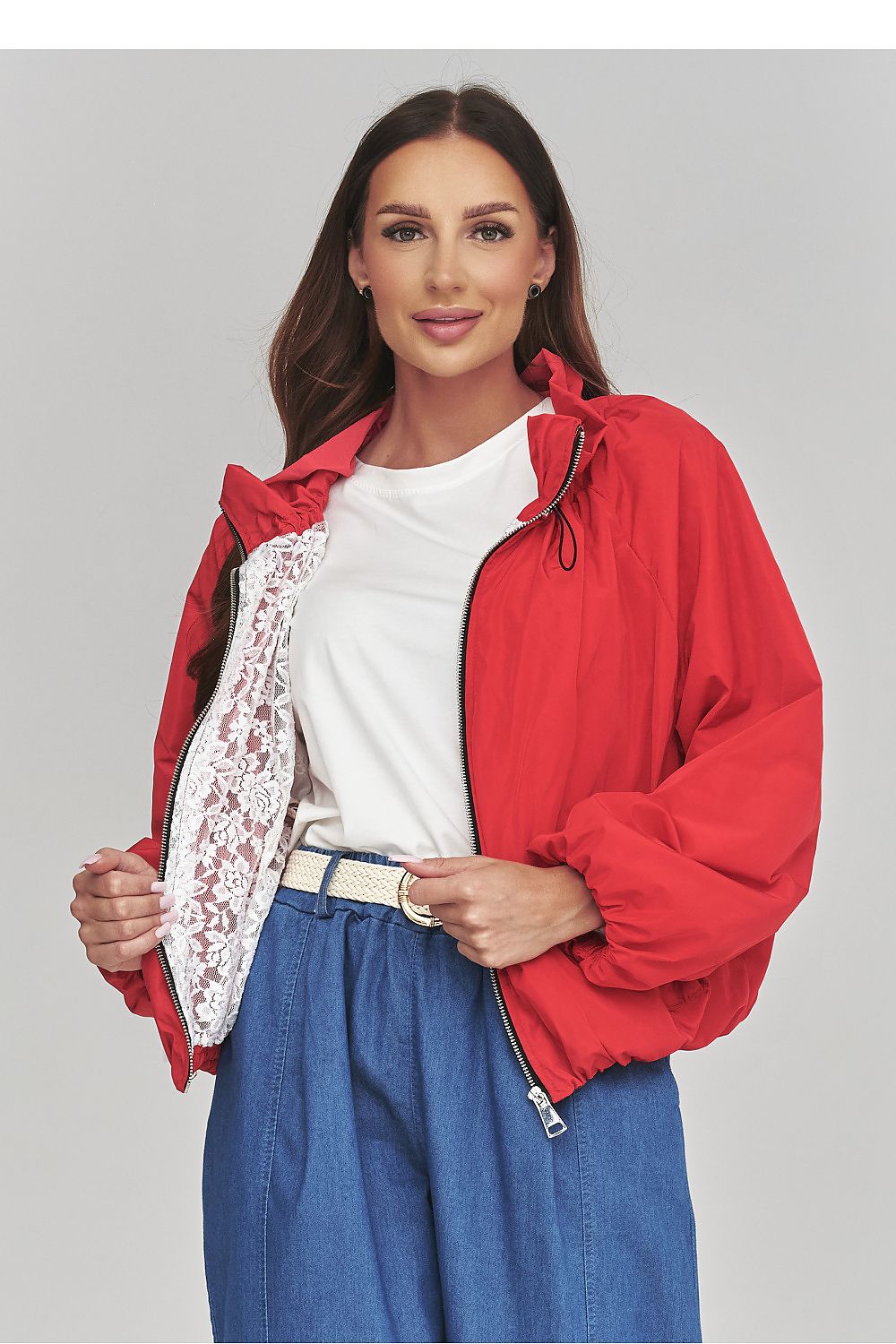 Woman wearing a red jacket over a white shirt with a floral pattern, standing against a plain background.