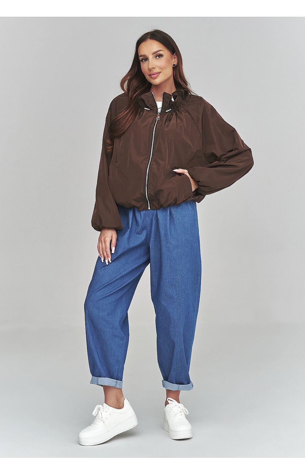 Woman wearing a brown jacket and blue pants on a gray background