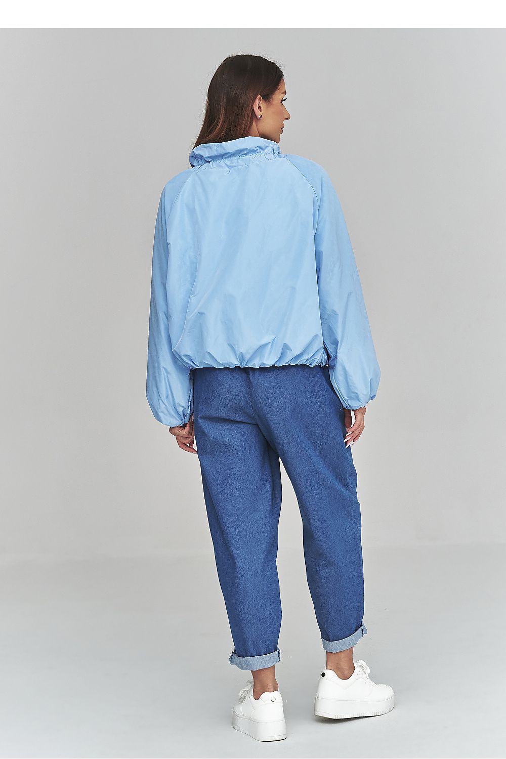 Person wearing a light blue jacket and blue jeans on a gray background