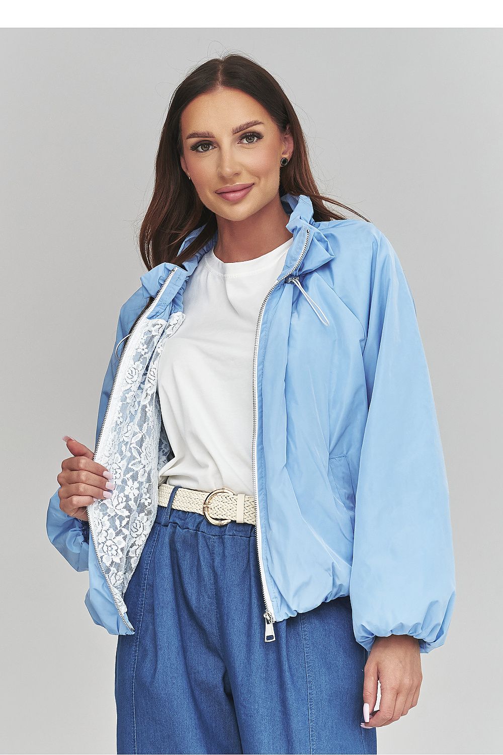 Woman wearing a light blue jacket over a white shirt and blue pants on a gray background