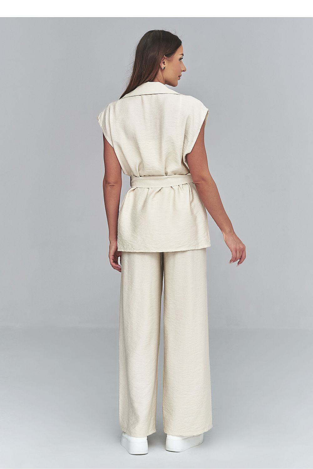 Woman wearing a beige sleeveless top and wide-leg pants on a gray background