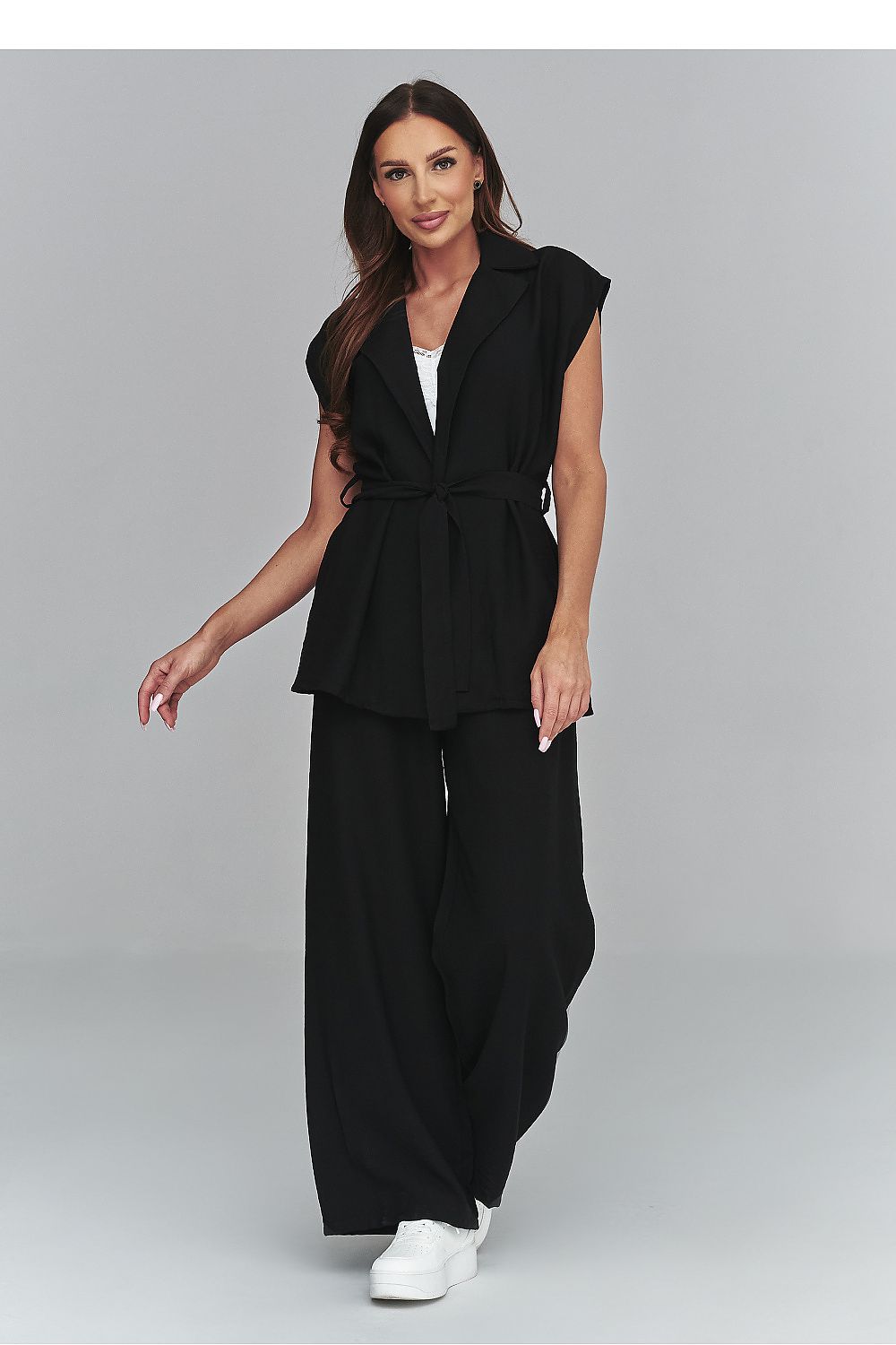 Woman wearing a black sleeveless blazer and wide-leg pants on a gray background