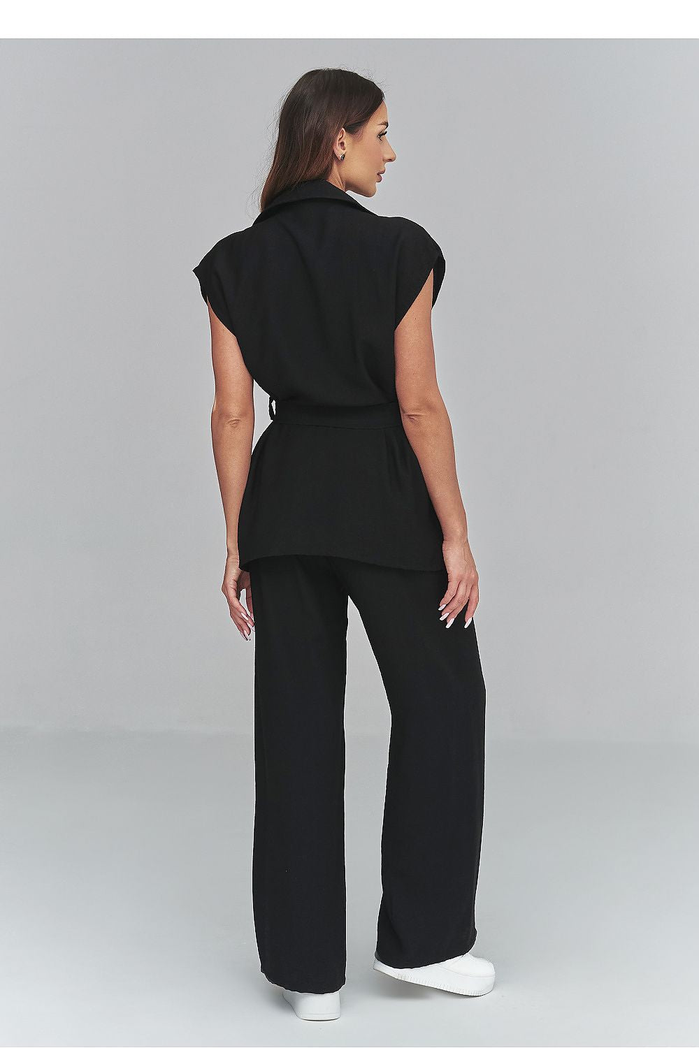 Woman wearing a black outfit with a belt on a gray background