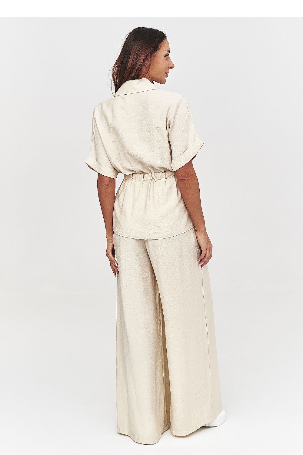 Woman wearing a beige outfit with wide-leg pants on a white background