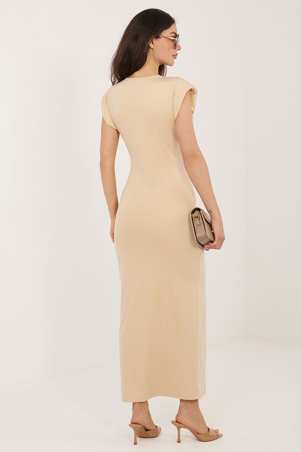 Woman wearing a beige dress holding a clutch against a white background