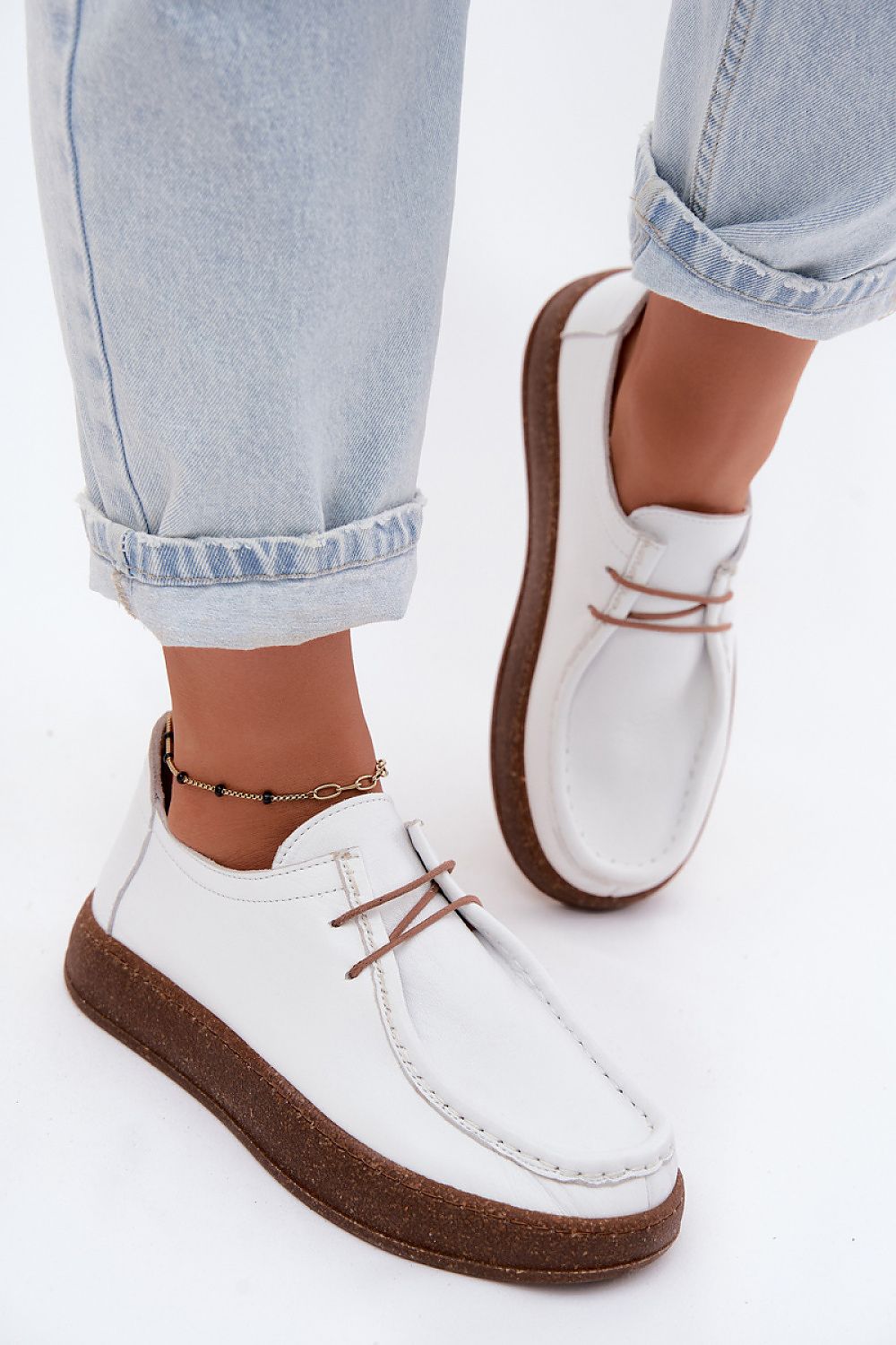 White loafers with brown soles worn with light blue jeans on a white background