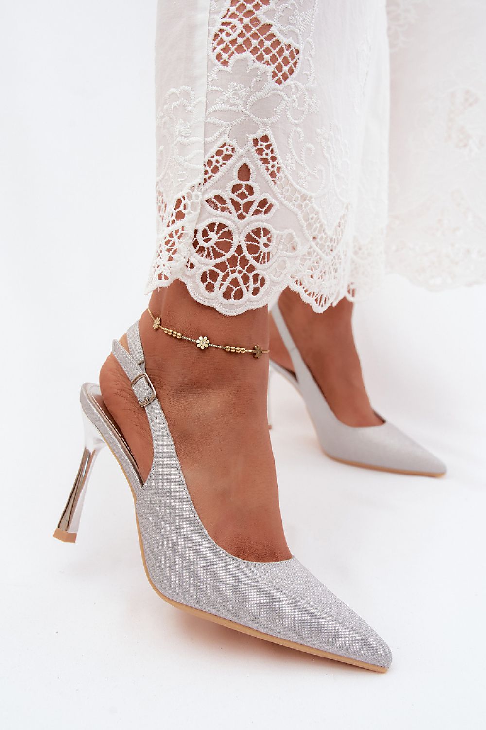 White high-heeled shoes worn with a lace dress on a white background