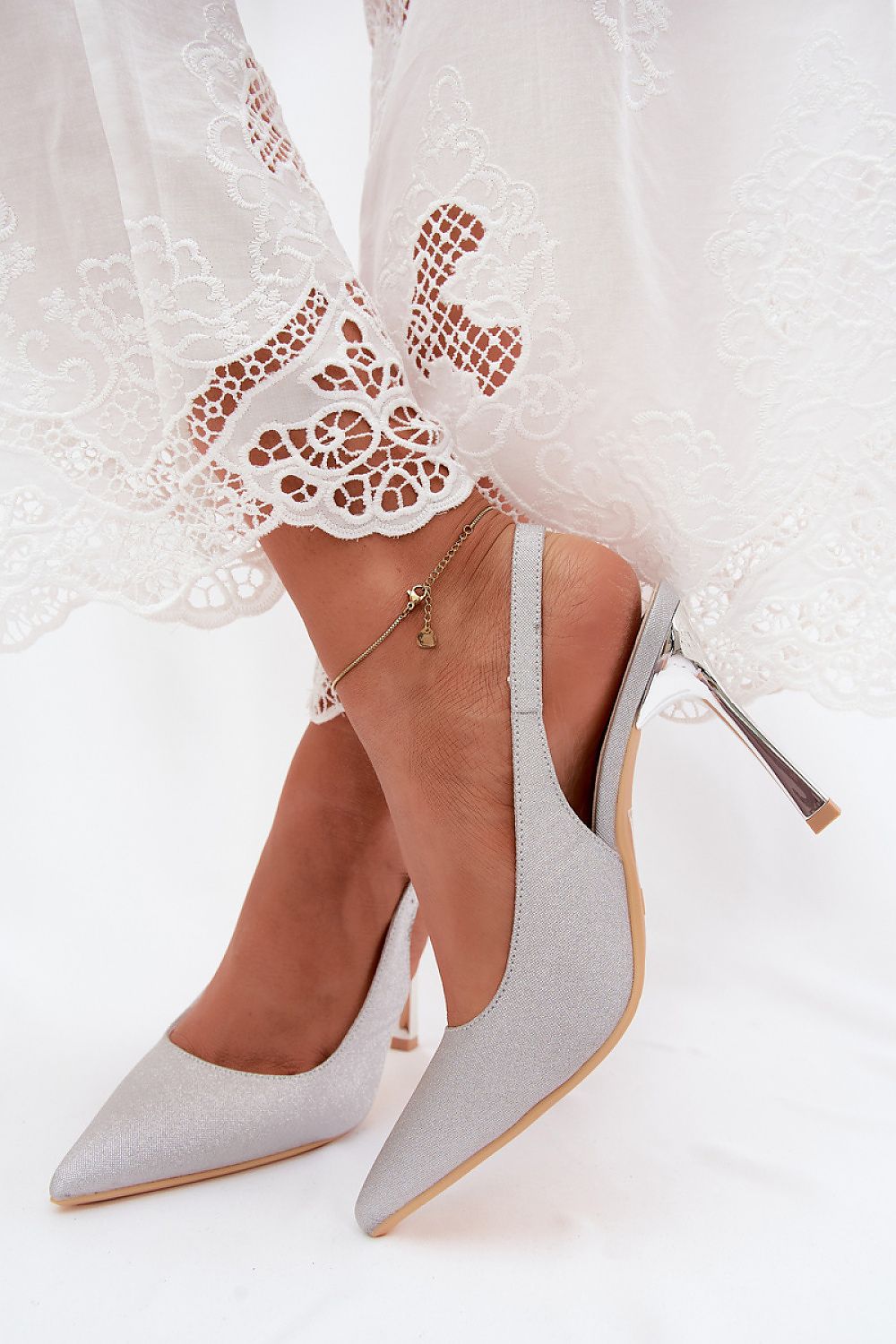 Gray high-heeled shoes worn with a white lace dress on a white background