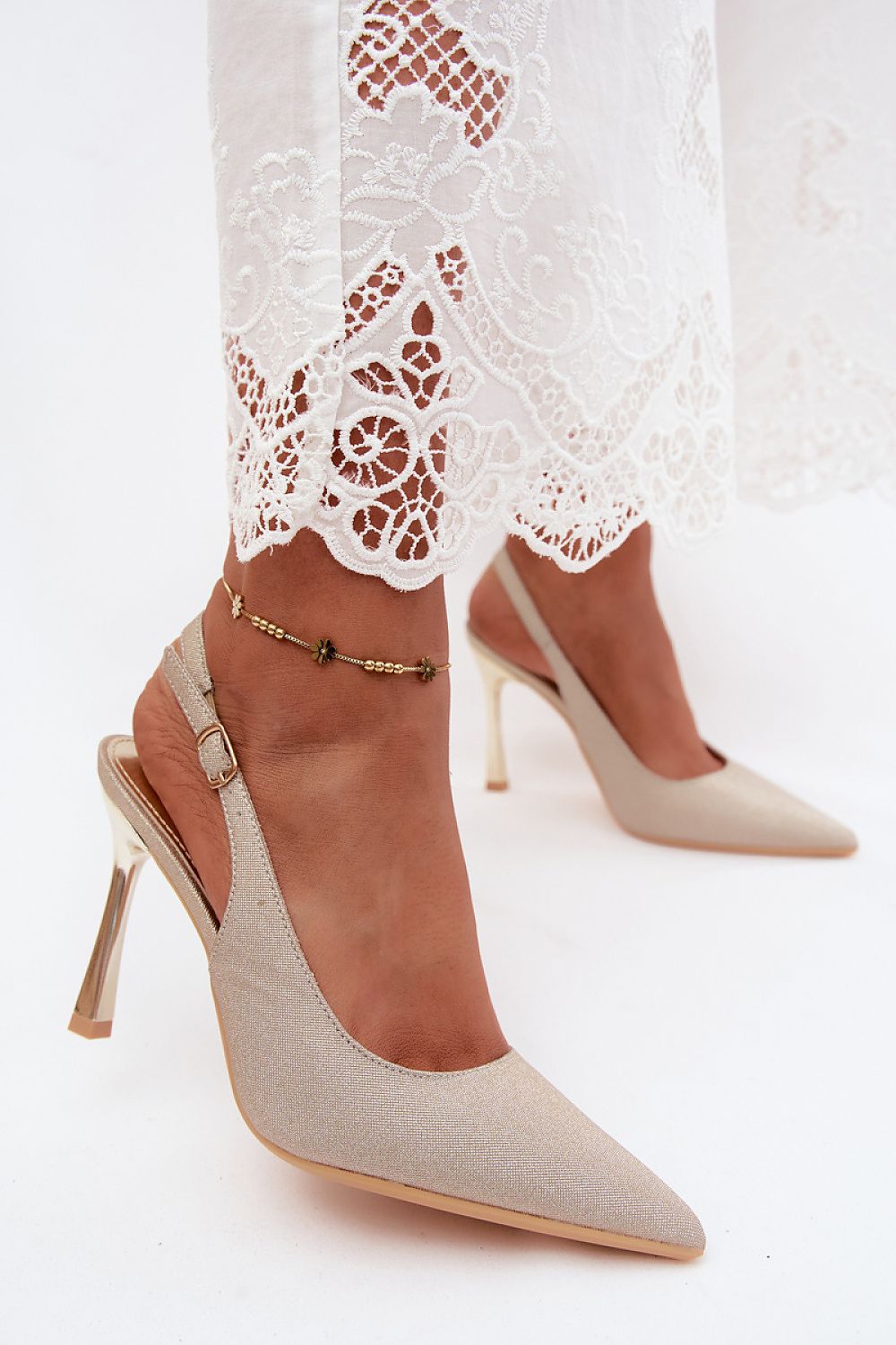 Pair of beige high-heeled shoes worn with a white lace dress on a light background