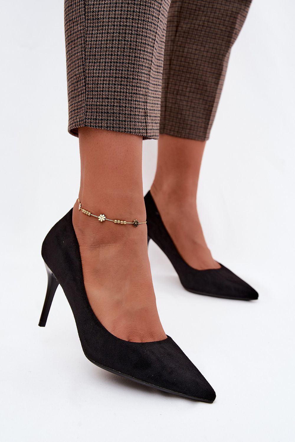 Black high-heeled shoes worn with plaid pants on a white background