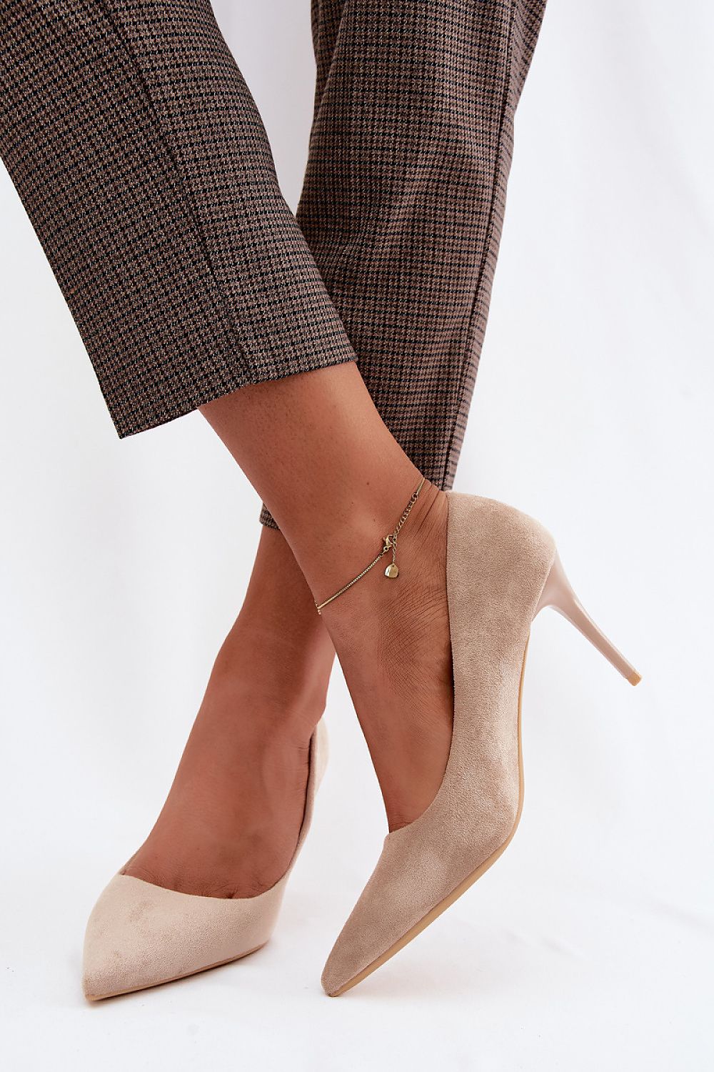 Beige suede high-heeled shoes worn with plaid pants on a white background