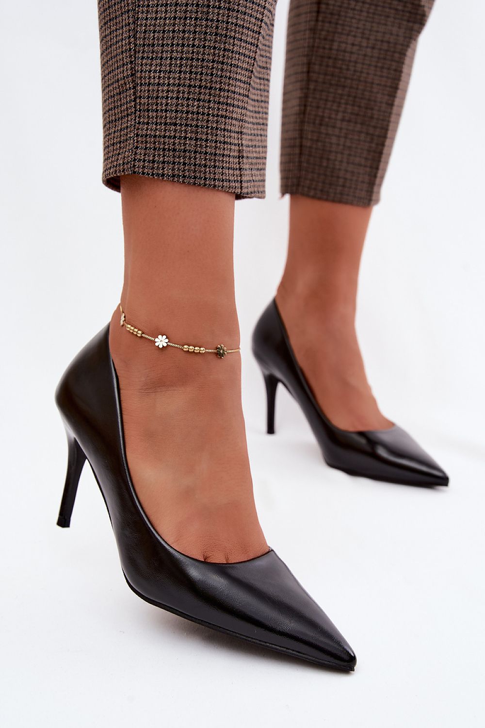 Black high-heeled shoes worn with plaid pants on a white background