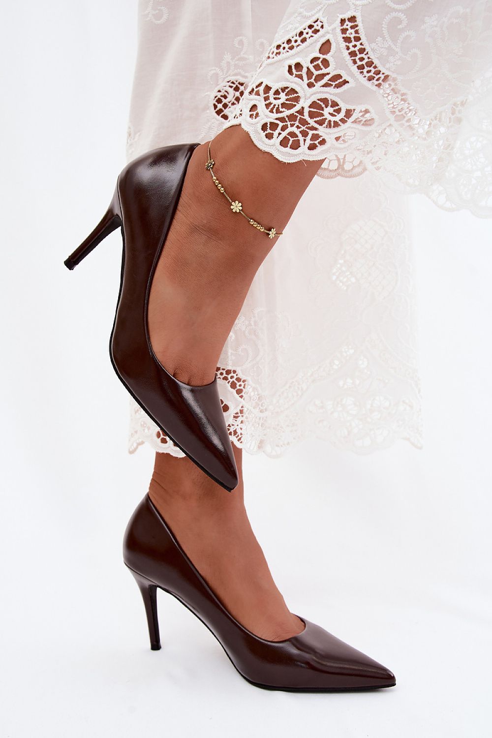Brown high-heeled shoes worn with a white lace garment on a light background