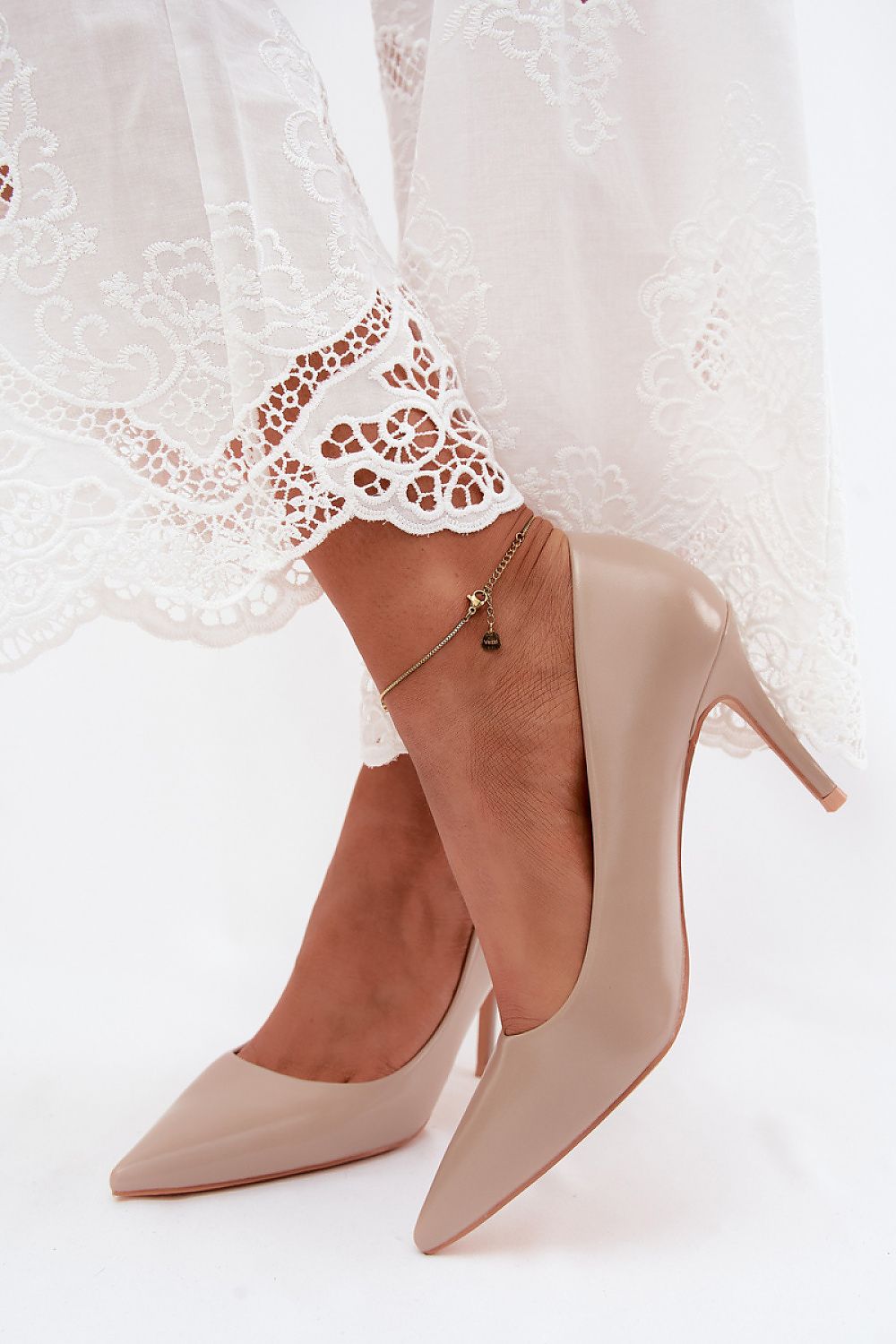 Beige high-heeled shoes worn with a white lace dress on a white background