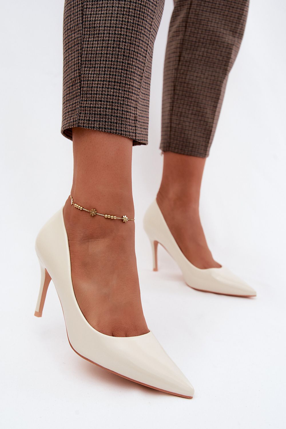 White high-heeled shoes worn with brown checkered pants on a white background