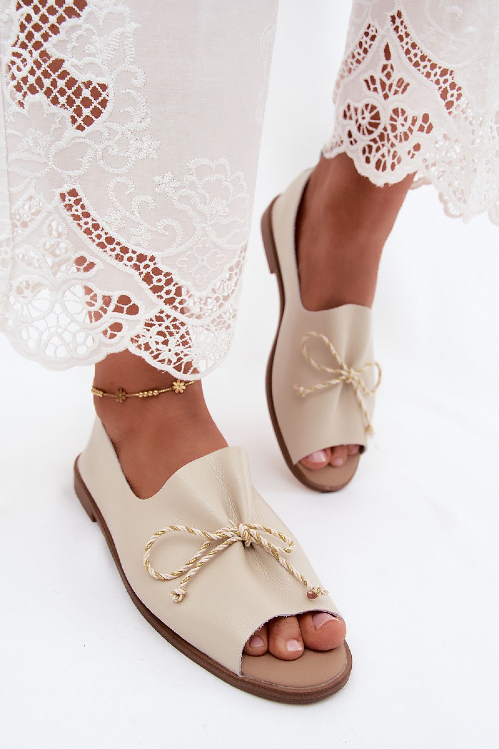 Beige open-toe sandals with lace details worn with a white lace dress.