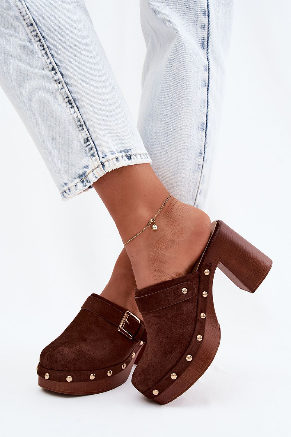 Brown suede clogs with gold studs worn with light blue jeans on a white background