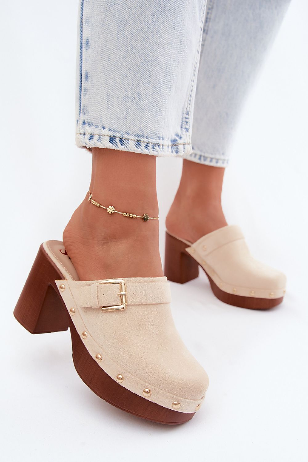 Beige clogs with brown soles worn with light blue jeans on a white background