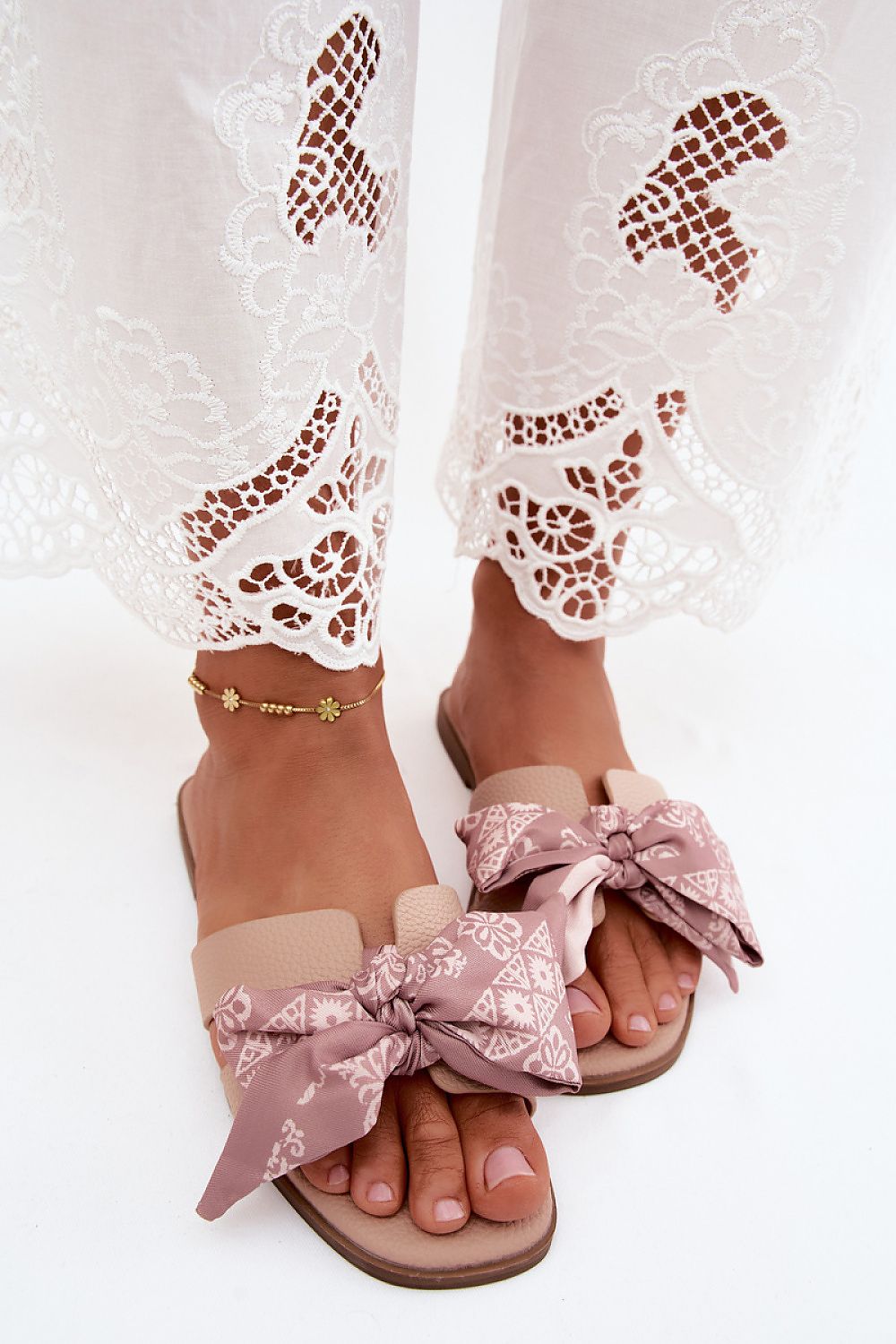 Pink sandals with floral straps worn with white lace pants on a light background