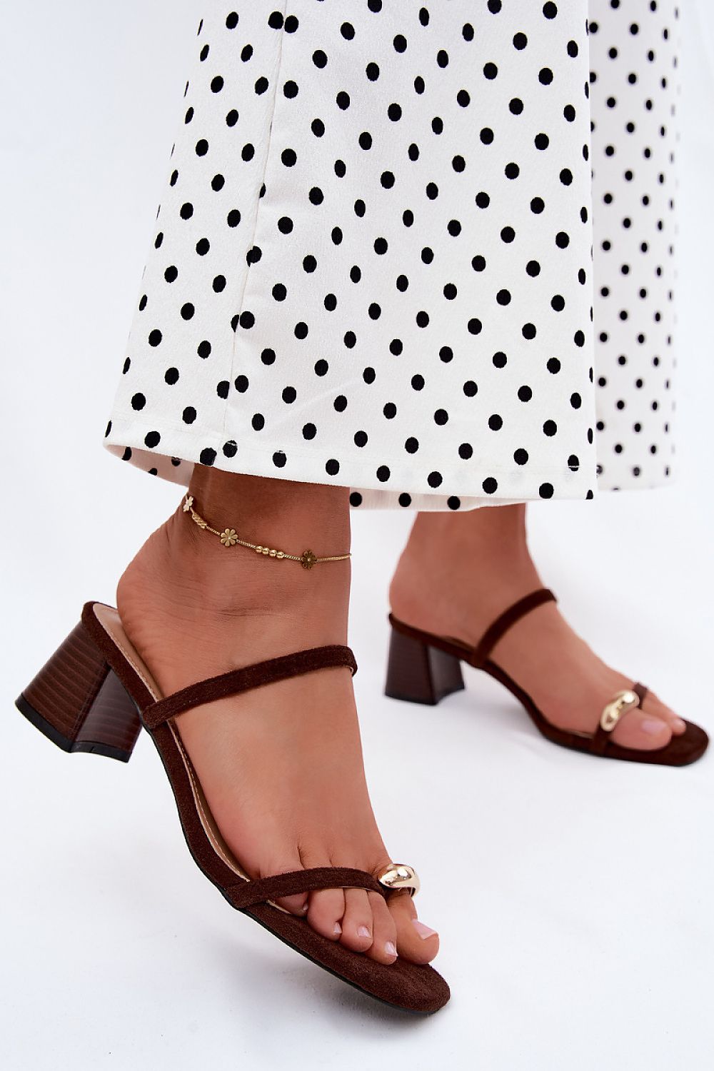 Brown block-heel sandals worn with a white skirt featuring black polka dots on a light gray background.