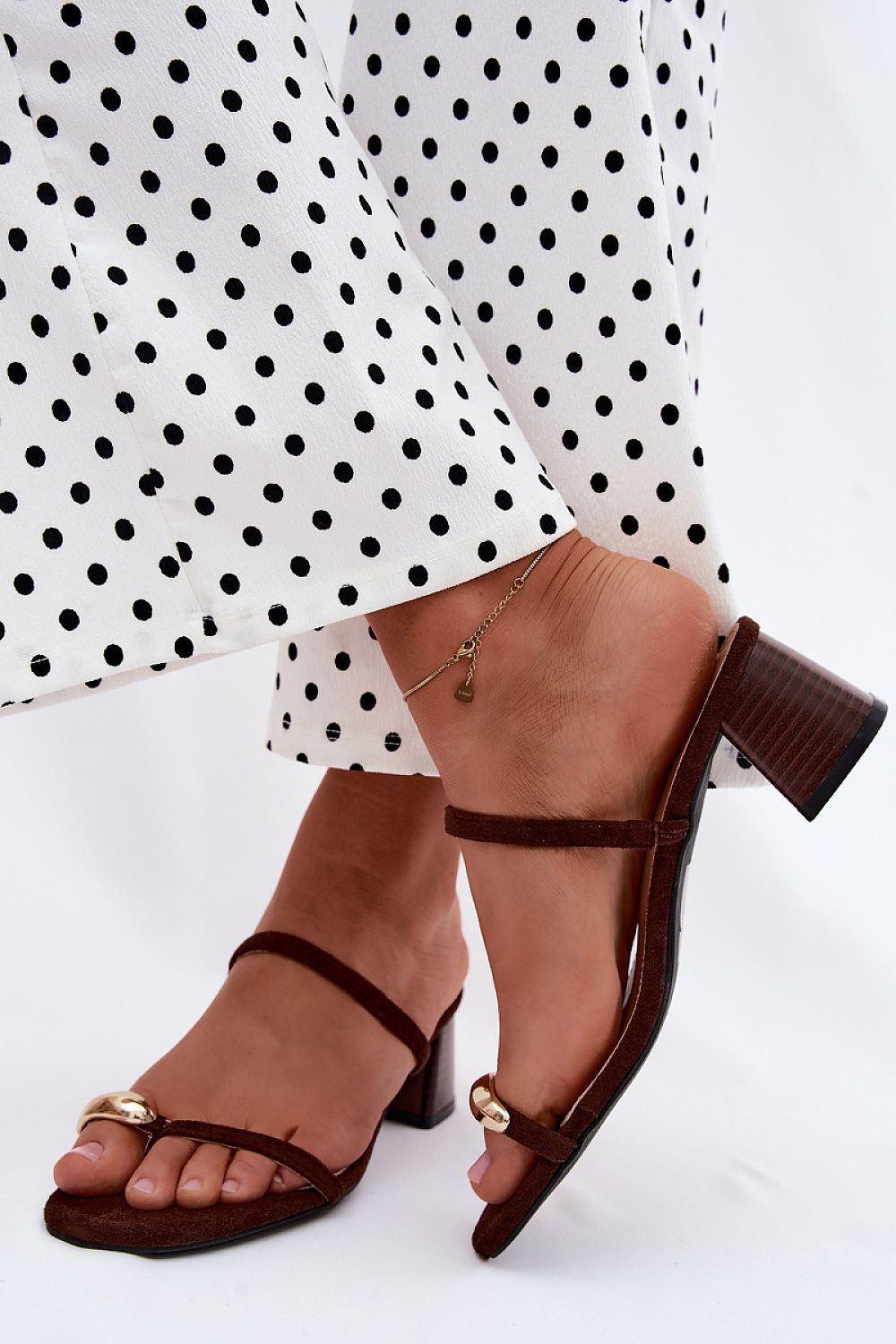 Brown sandals worn with a white polka dot dress on a white background