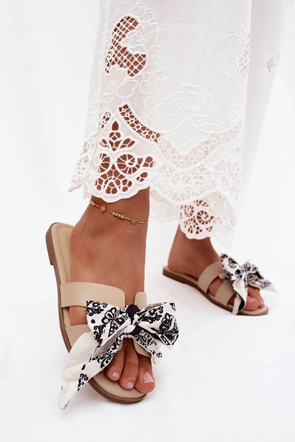 Beige sandals with decorative bows worn with a white lace dress on a white background