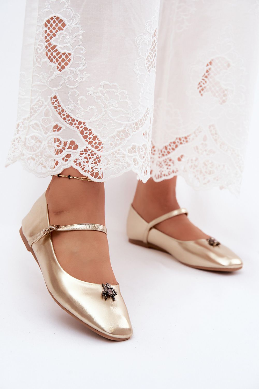 Gold ballet flats worn with white lace pants on a light background