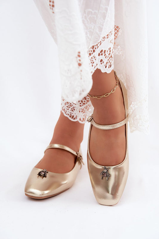 Gold ballet flats worn with white lace pants on a white background