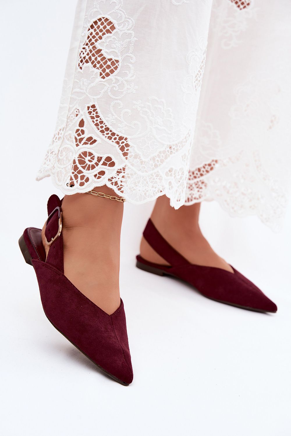 Maroon pointed-toe shoes worn with a white lace dress on a light background