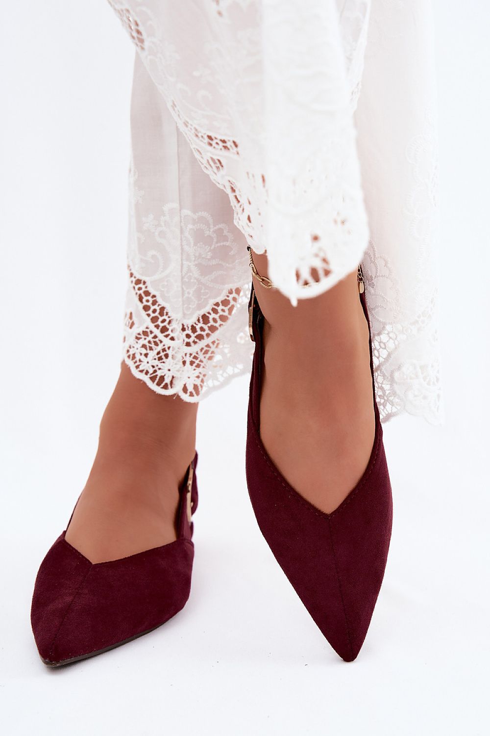 Burgundy pointed-toe shoes worn with a white lace dress on a white background