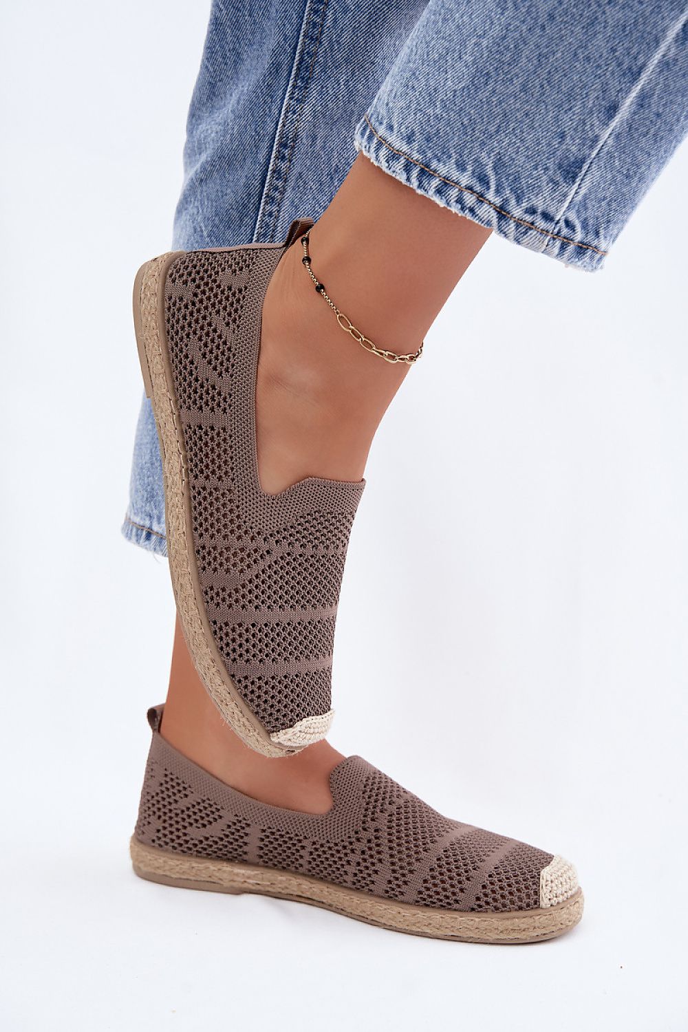 Brown perforated espadrille shoes worn with rolled-up jeans on a light gray background