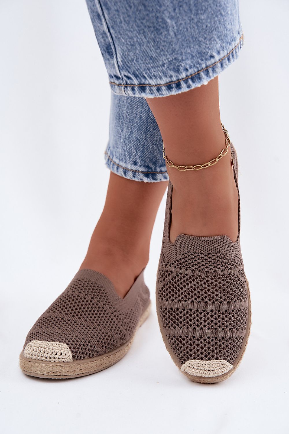 Brown woven espadrilles worn with blue jeans on a white background