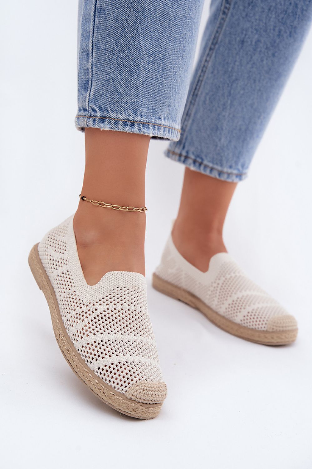White knit slip-on shoes worn with light blue jeans on a white background