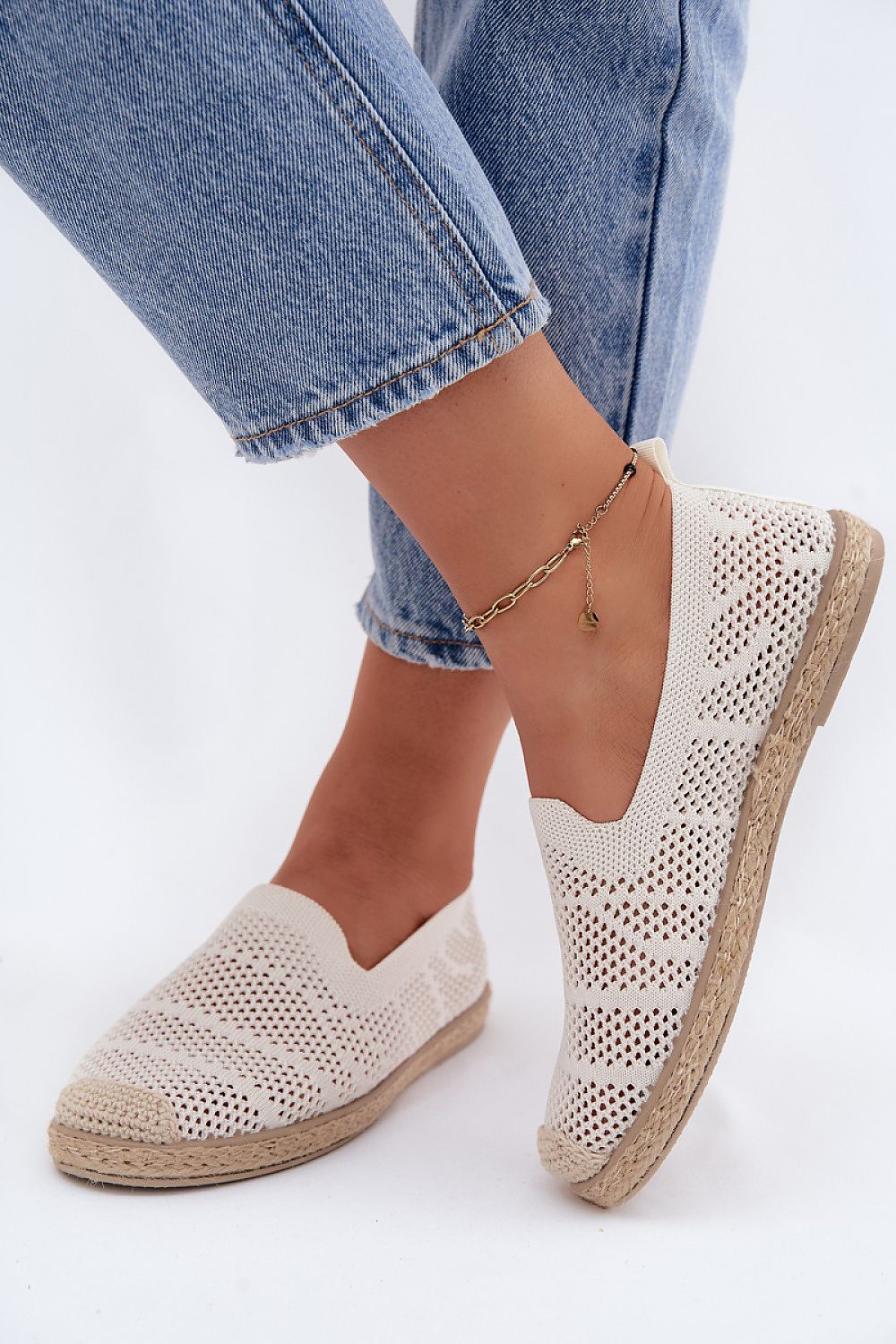 White perforated espadrilles worn with blue jeans on a white background