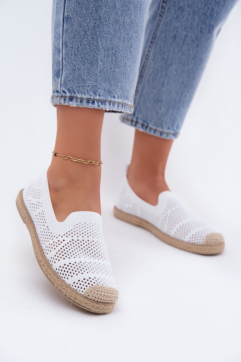 White woven shoes with brown soles worn with light blue jeans on a white background