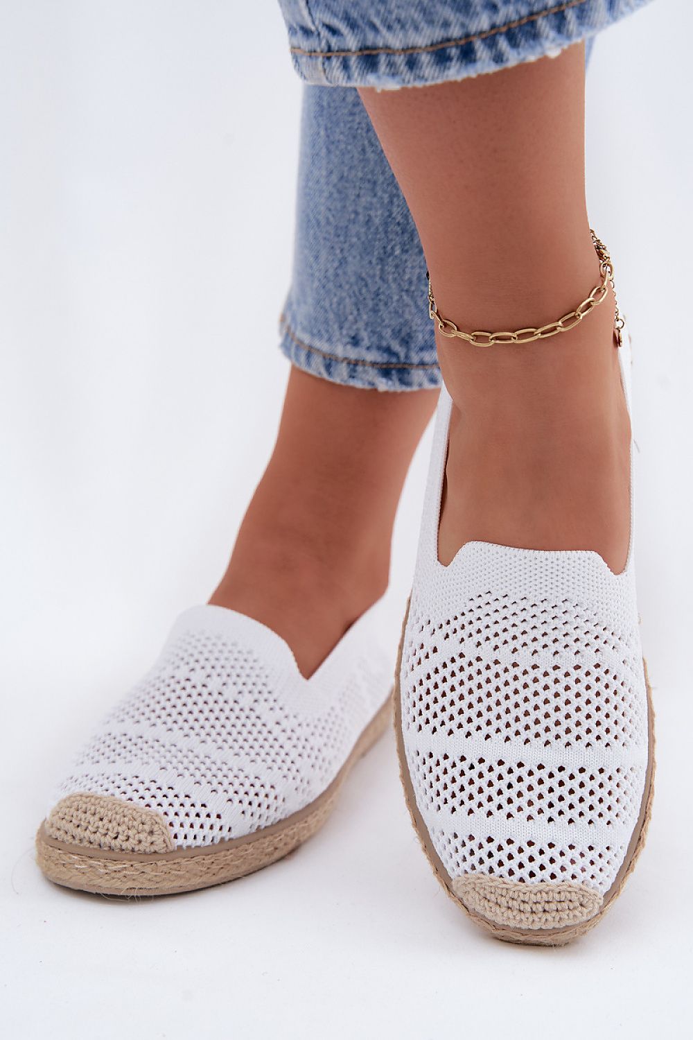 White woven espadrilles worn with blue jeans on a white background