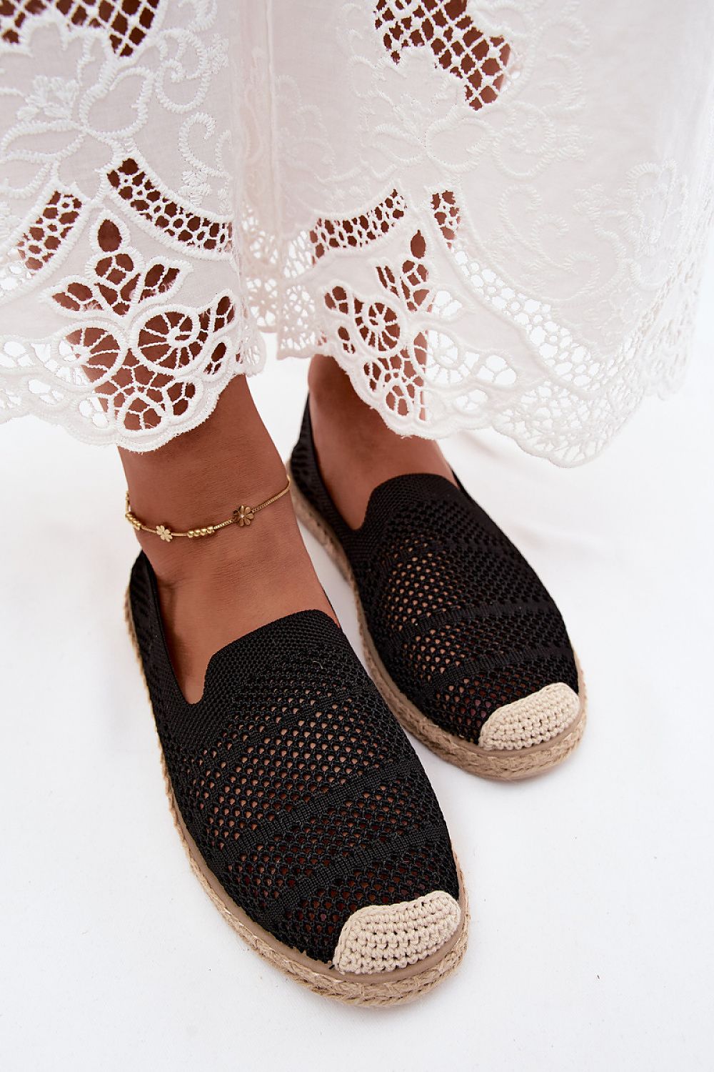 Black woven espadrilles with beige soles worn with a white lace dress.