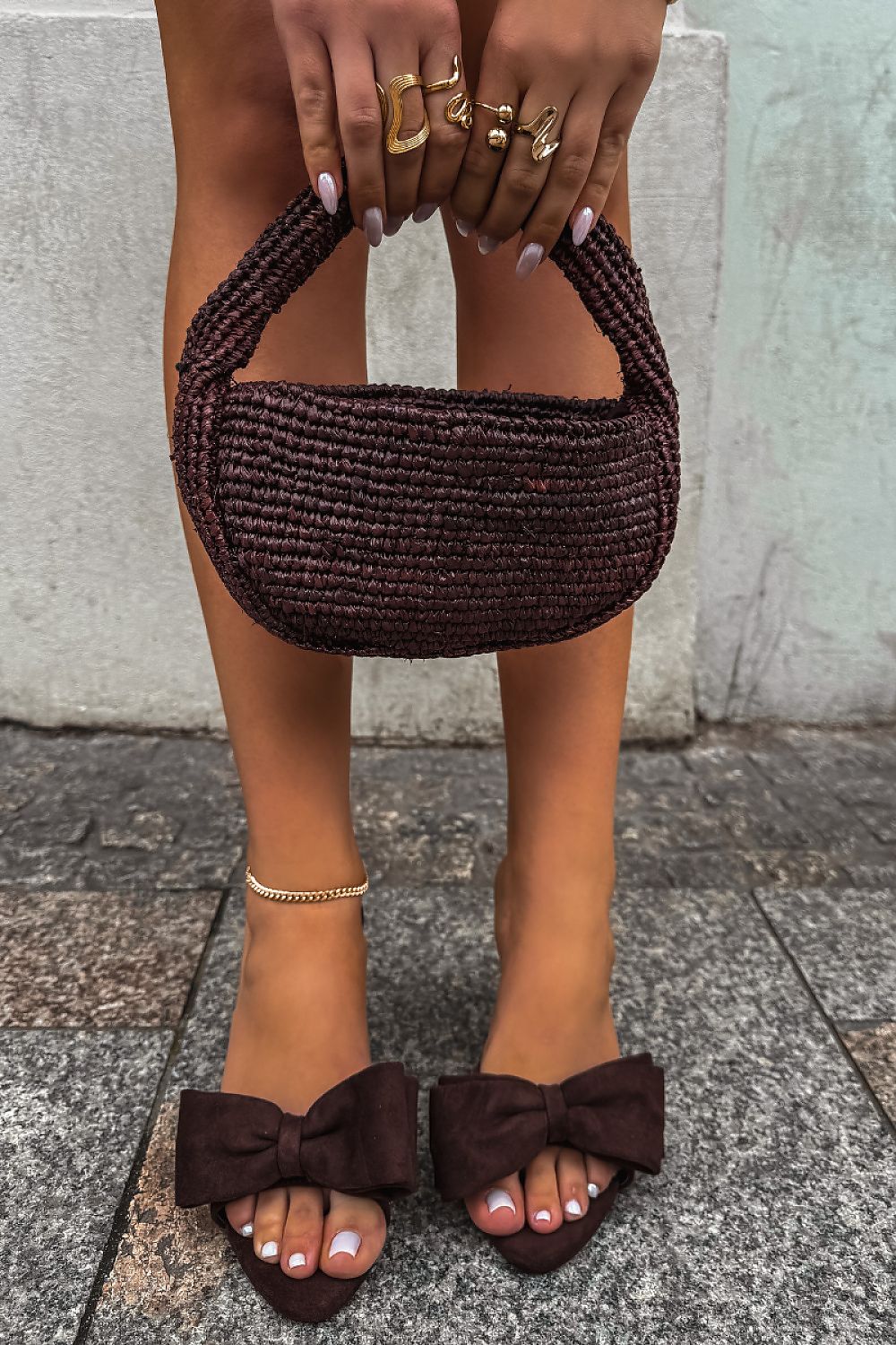 Person holding a brown woven handbag with matching shoes on a pavement background