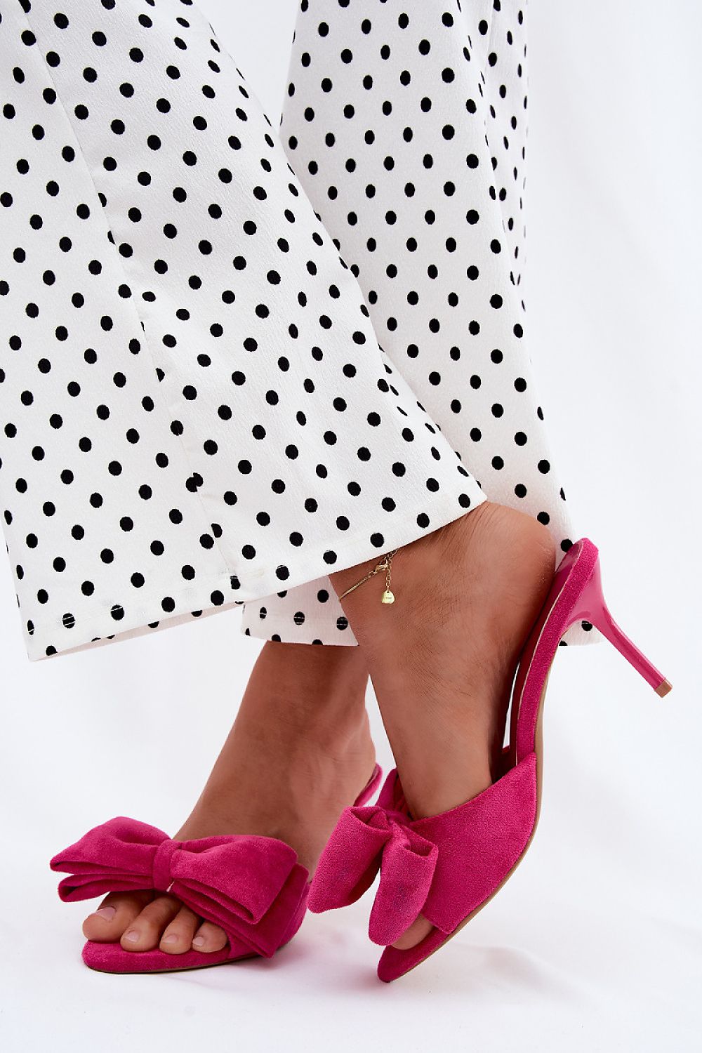 Pink high-heeled shoes with bow details worn with a white polka dot dress.