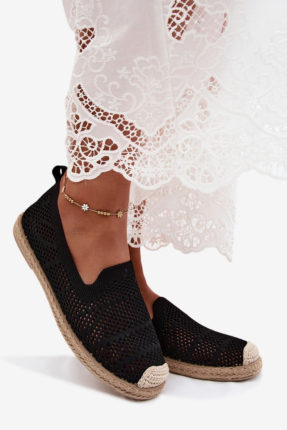 Black woven espadrille shoes worn with a white lace dress on a white background