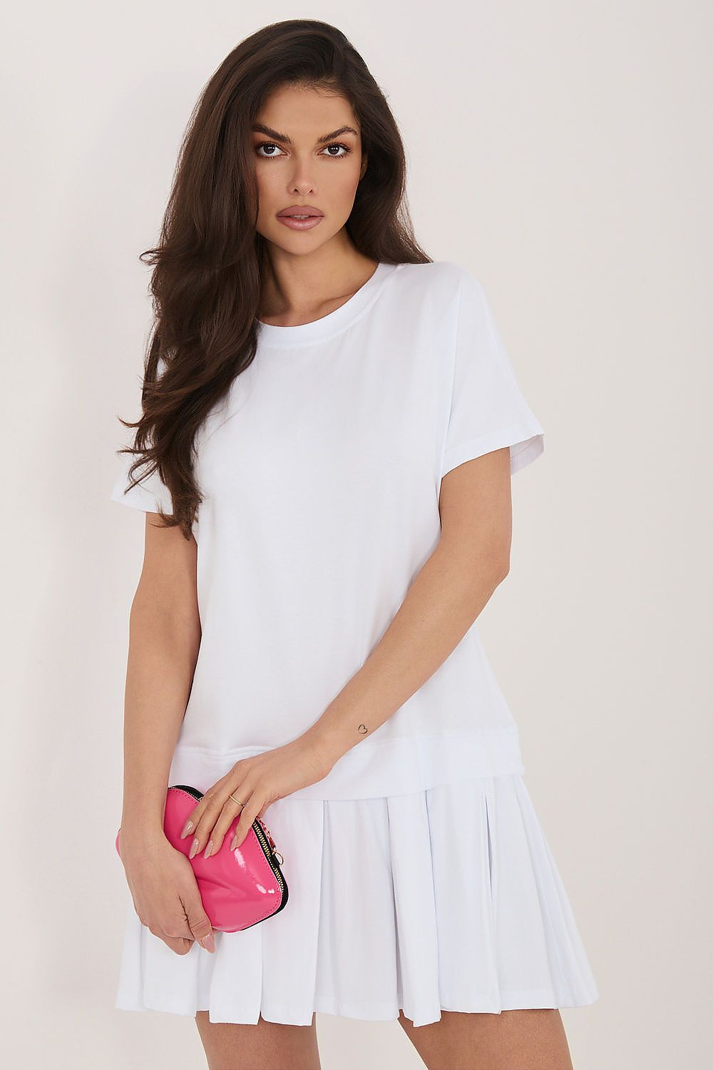 Woman wearing a white dress holding a pink clutch against a plain background