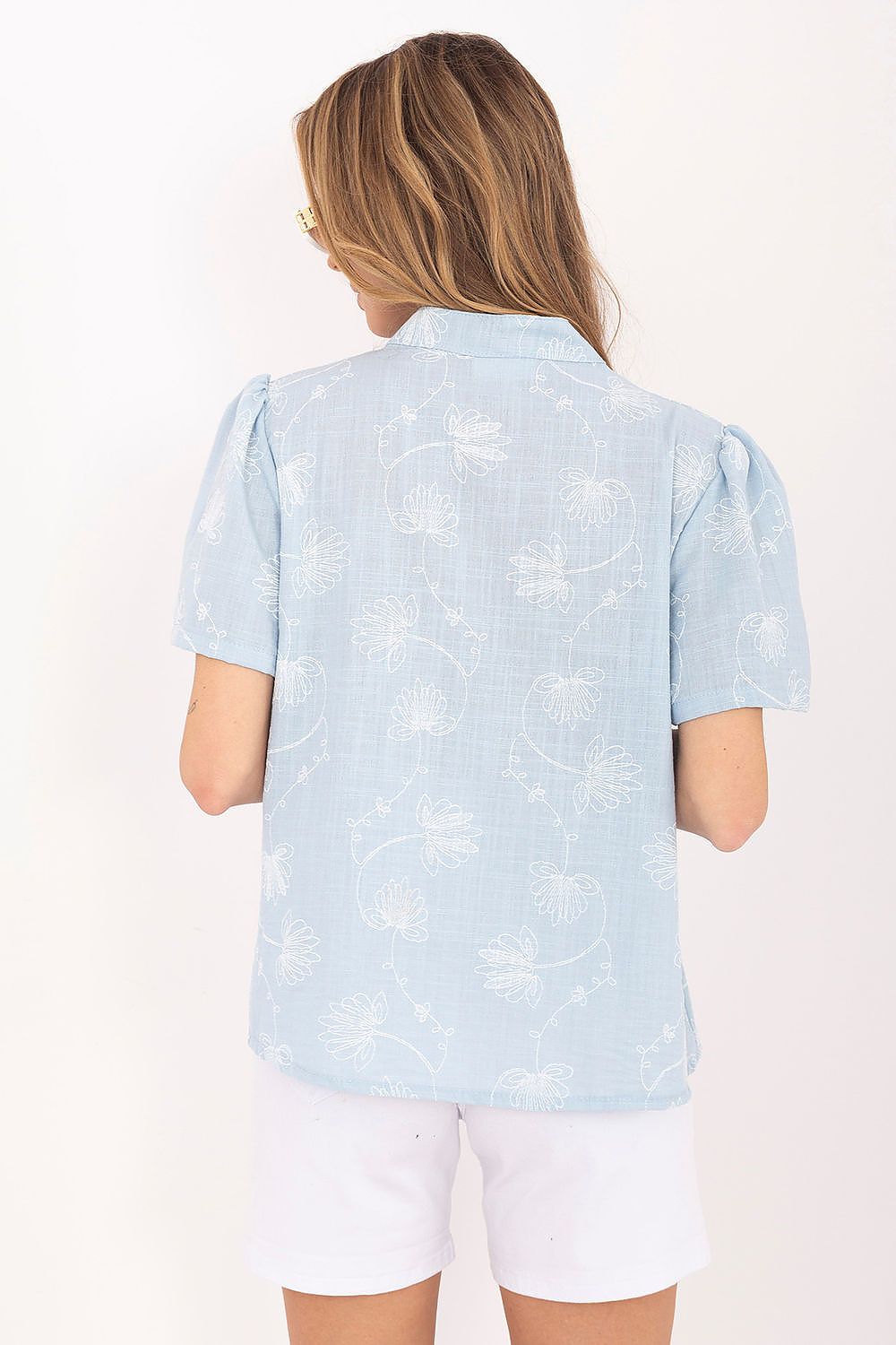 Person wearing a light blue patterned shirt and white shorts on a plain background