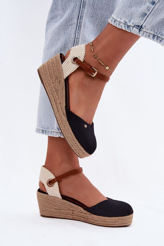 Black and beige wedge sandals with espadrille sole worn with light blue jeans on a white background
