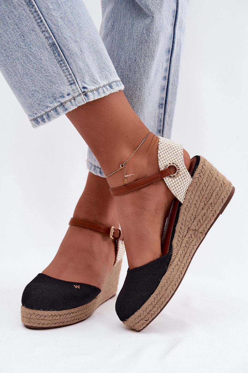 Black wedge sandals with brown straps worn with light blue jeans on a white background
