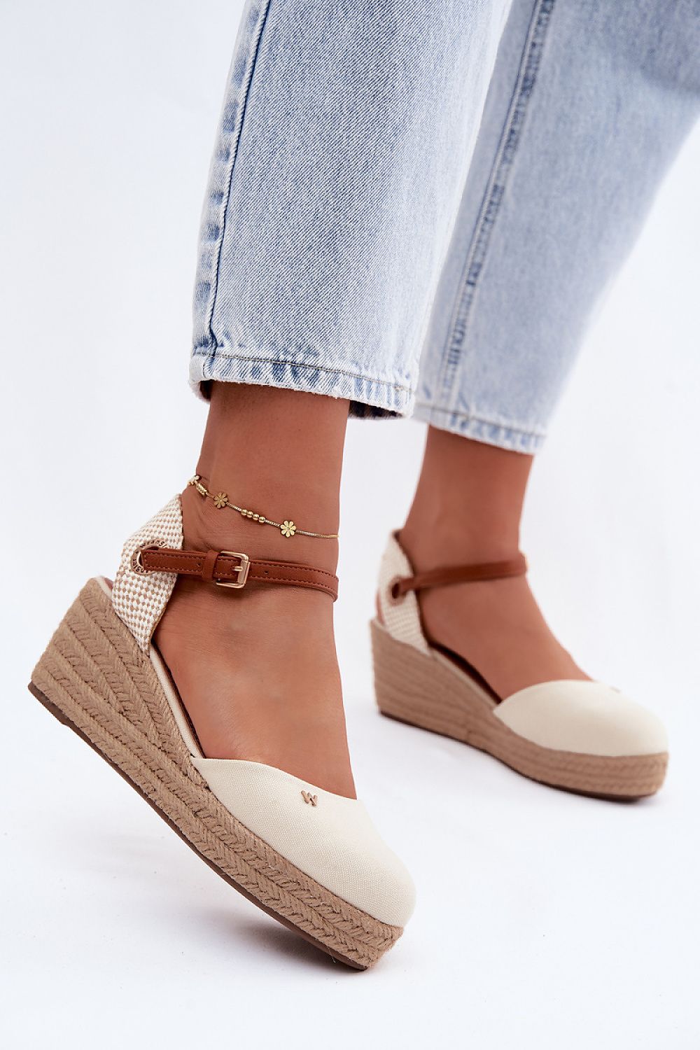 Beige wedge sandals with brown straps worn with light blue jeans on a white background