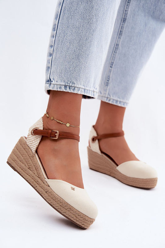 Beige wedge sandals with brown straps worn with light blue jeans on a white background