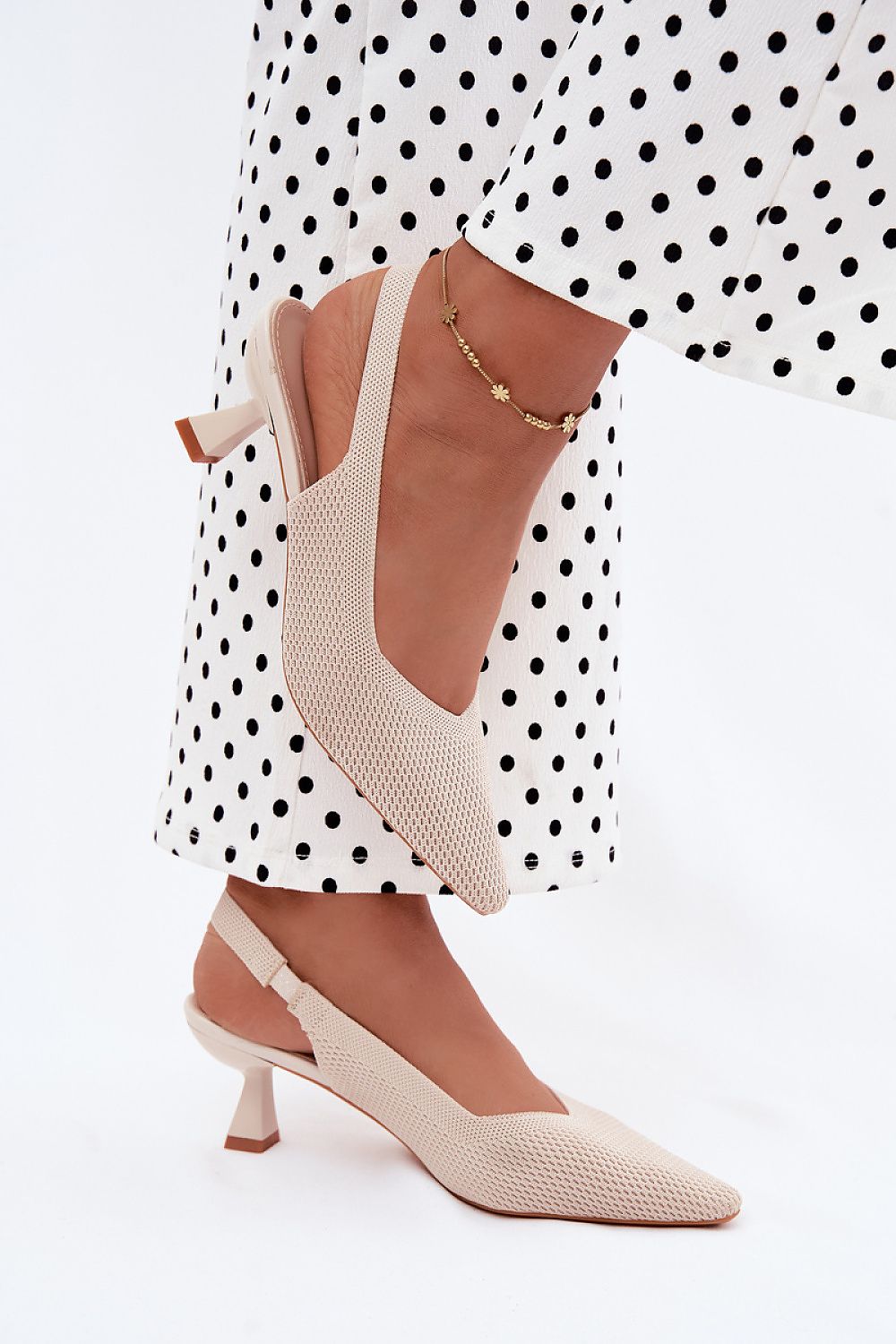 Beige high-heeled shoes worn with a polka dot dress on a white background