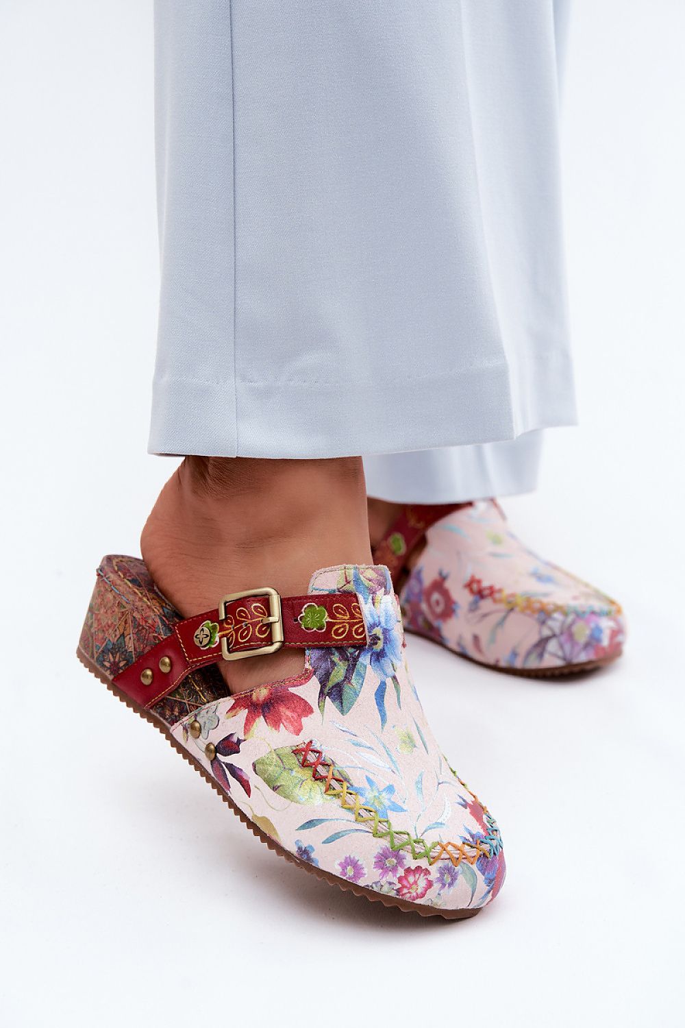 Colorful floral-patterned clogs with a red strap worn by a person on a white background