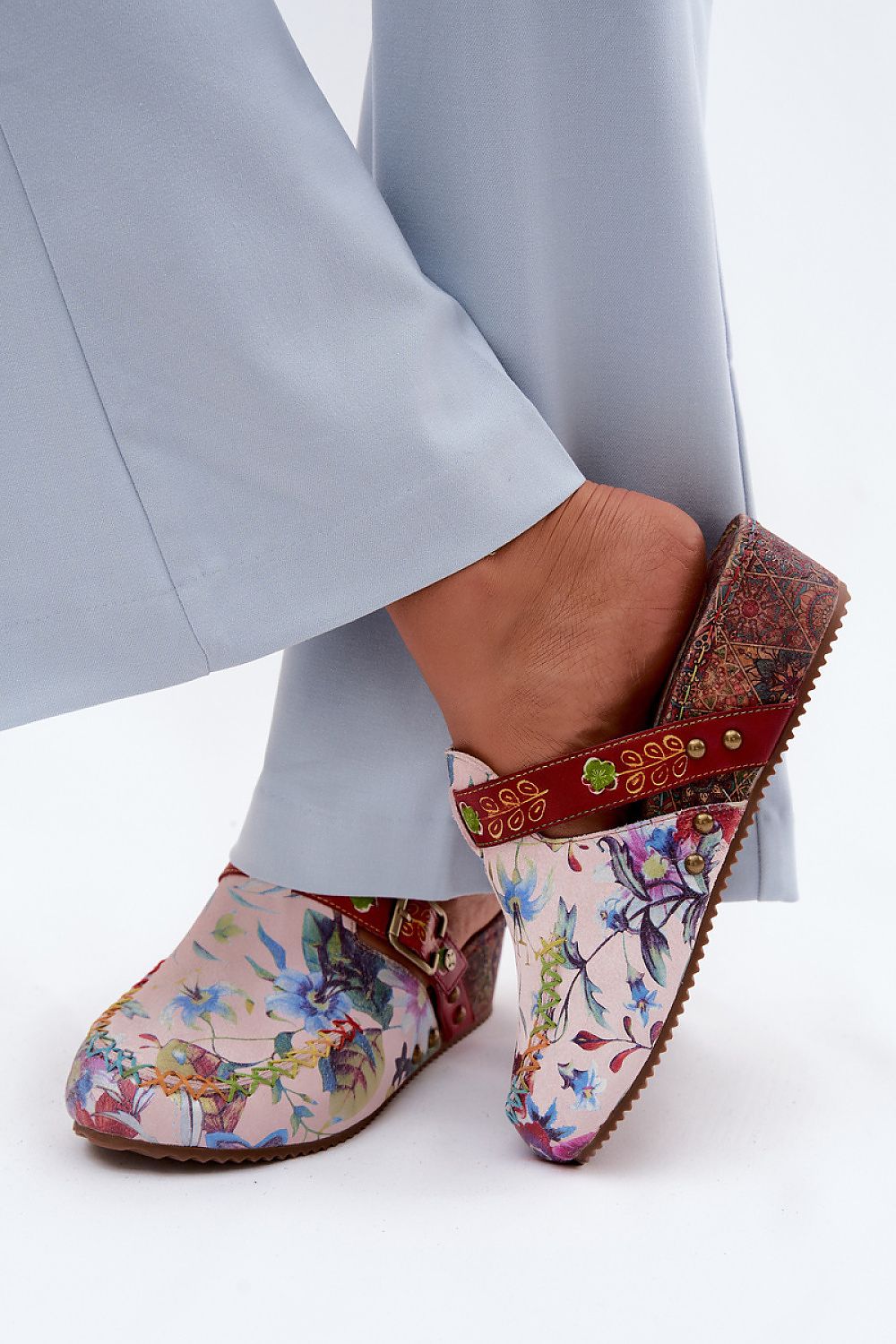 Colorful floral-patterned clogs worn with light gray pants on a white background